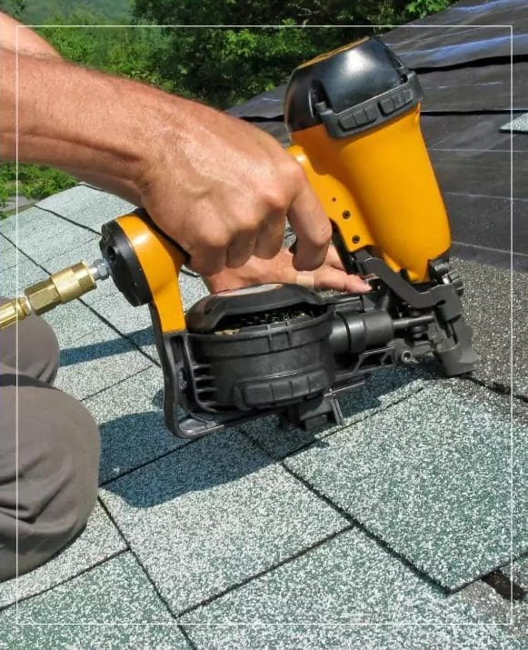 A man using a nail gun on a shingled roof.